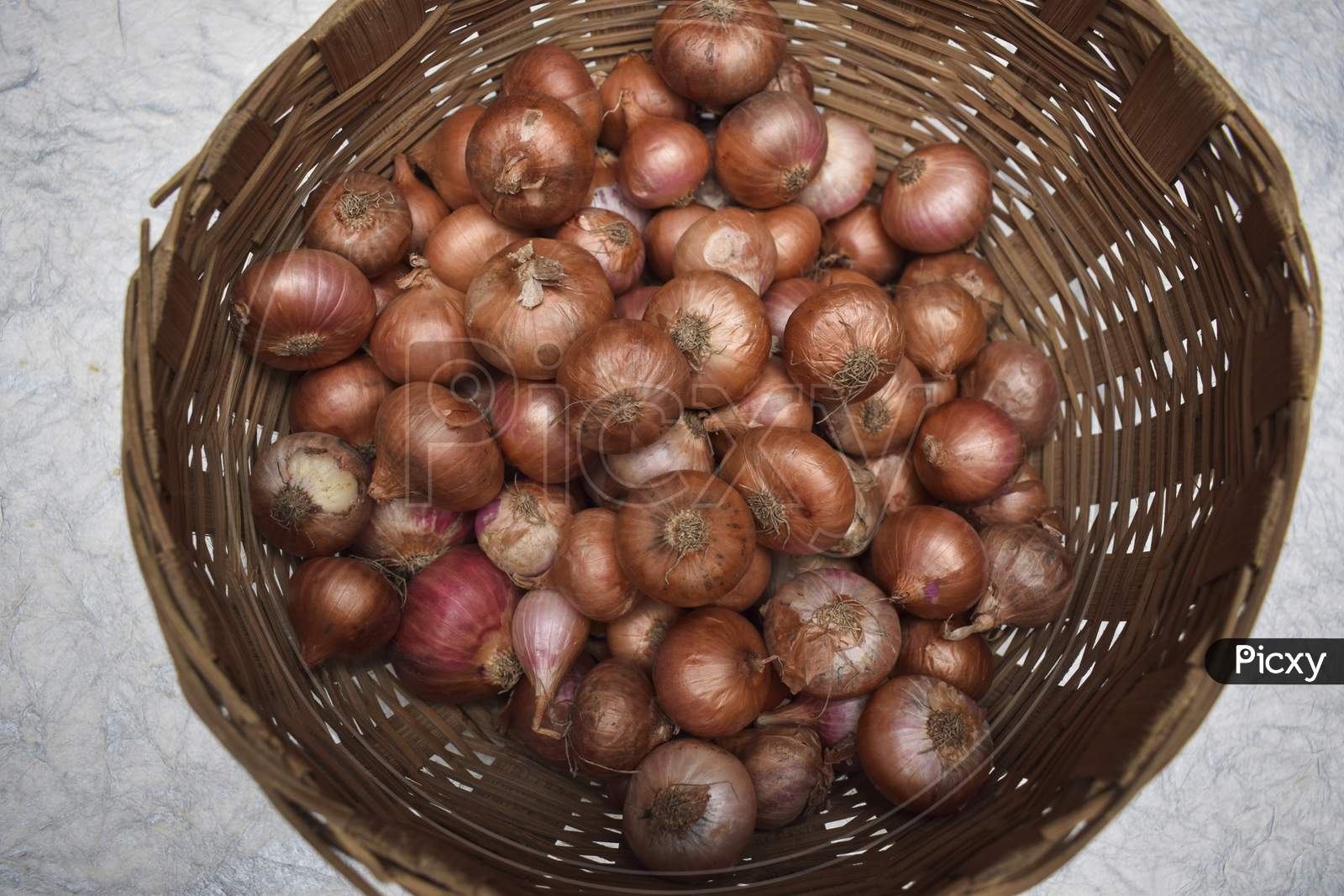 Top View Of Small Onions Stored In Round Brown Wicker Bamboo Basket In Indian And Pakistani Household.