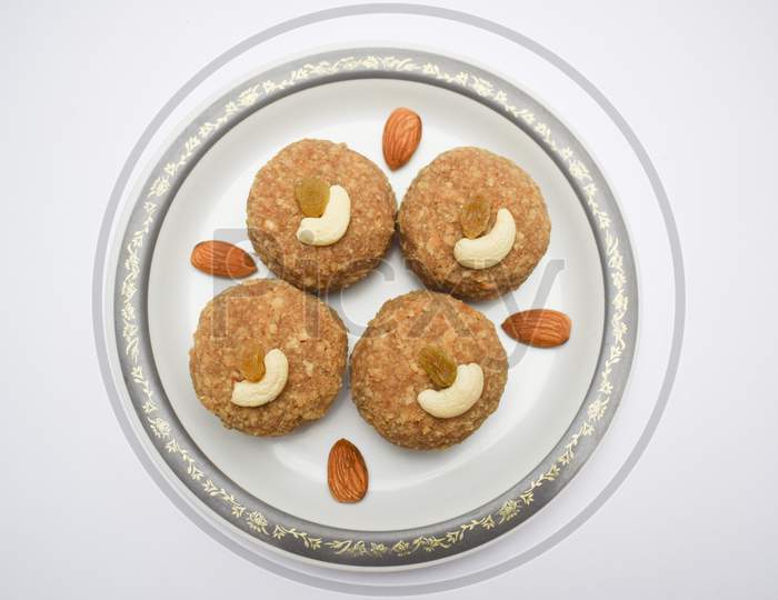 Top View Of Laddu, Ladoos Made Of Wheat Flour And Clarified Butter Ghee Served In Plate During Festival Like Ganesh Chaturthi Prasad, Diwali Decorated With Dryfruits Cashewnuts And Almonds On White
