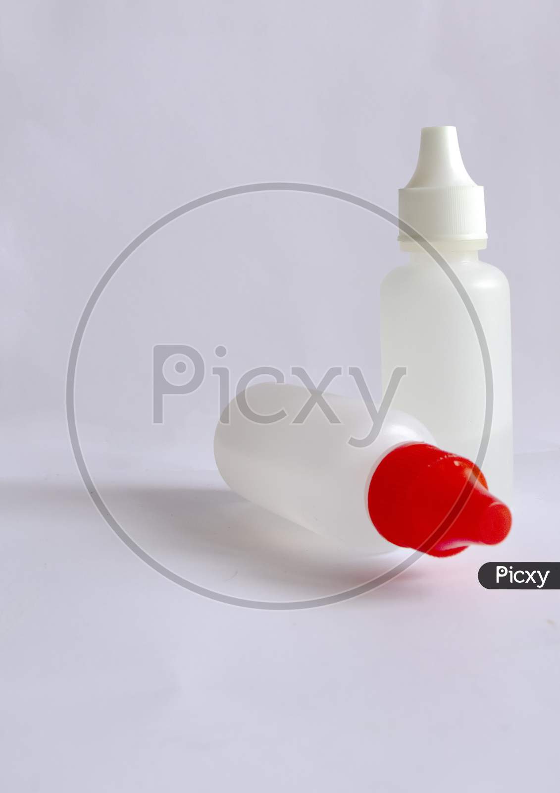 Two Small White Bottles With One White Cap And One With Red Cap On White Background.