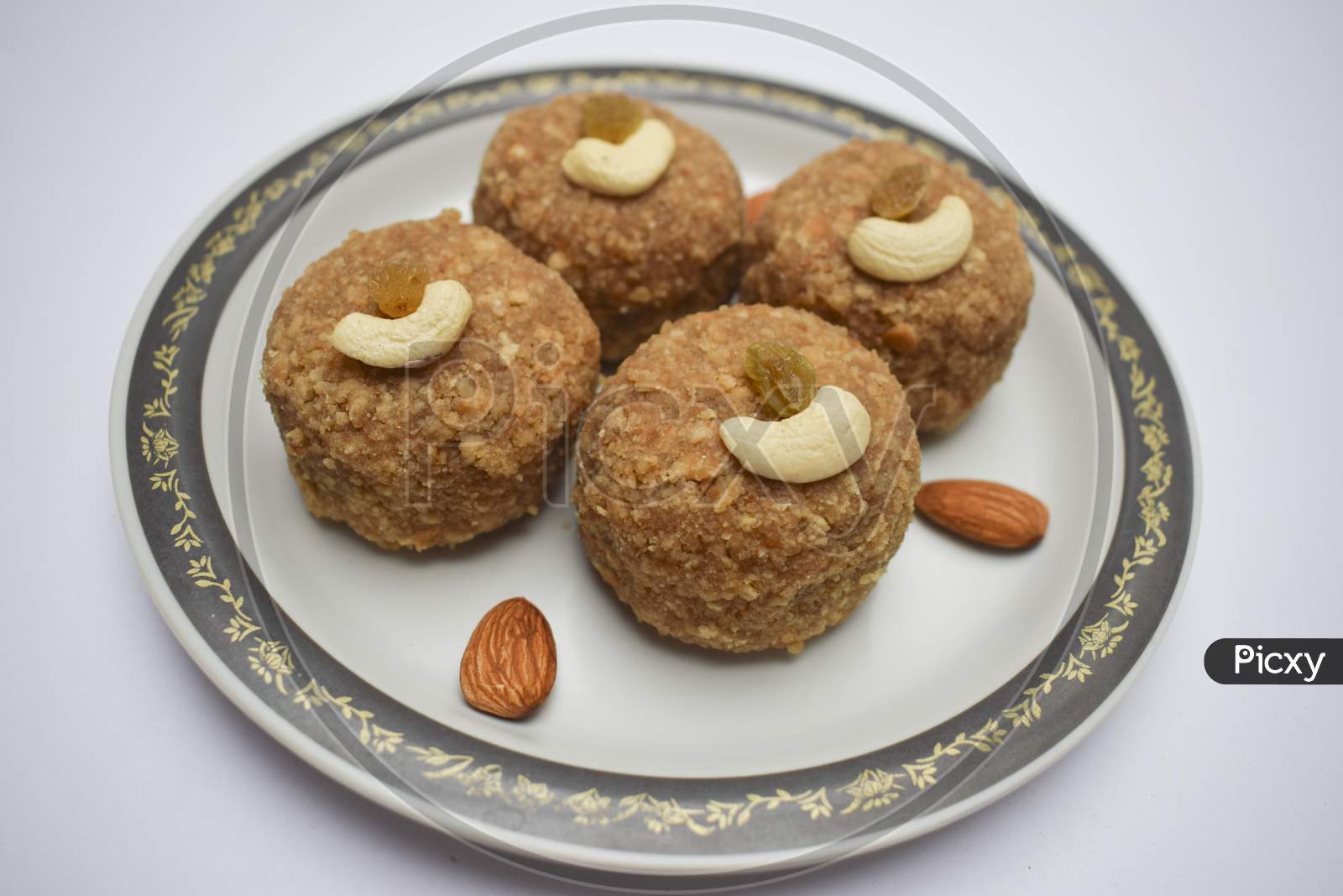 Closeup Of Laddu Or Ladoos Made Of Wheat Flour And Clarified Butter Ghee Served In Plate During Festival Like Ganesh Chaturthi Prasad, Diwali Decorated With Dryfruits Cashewnuts And Almonds On White