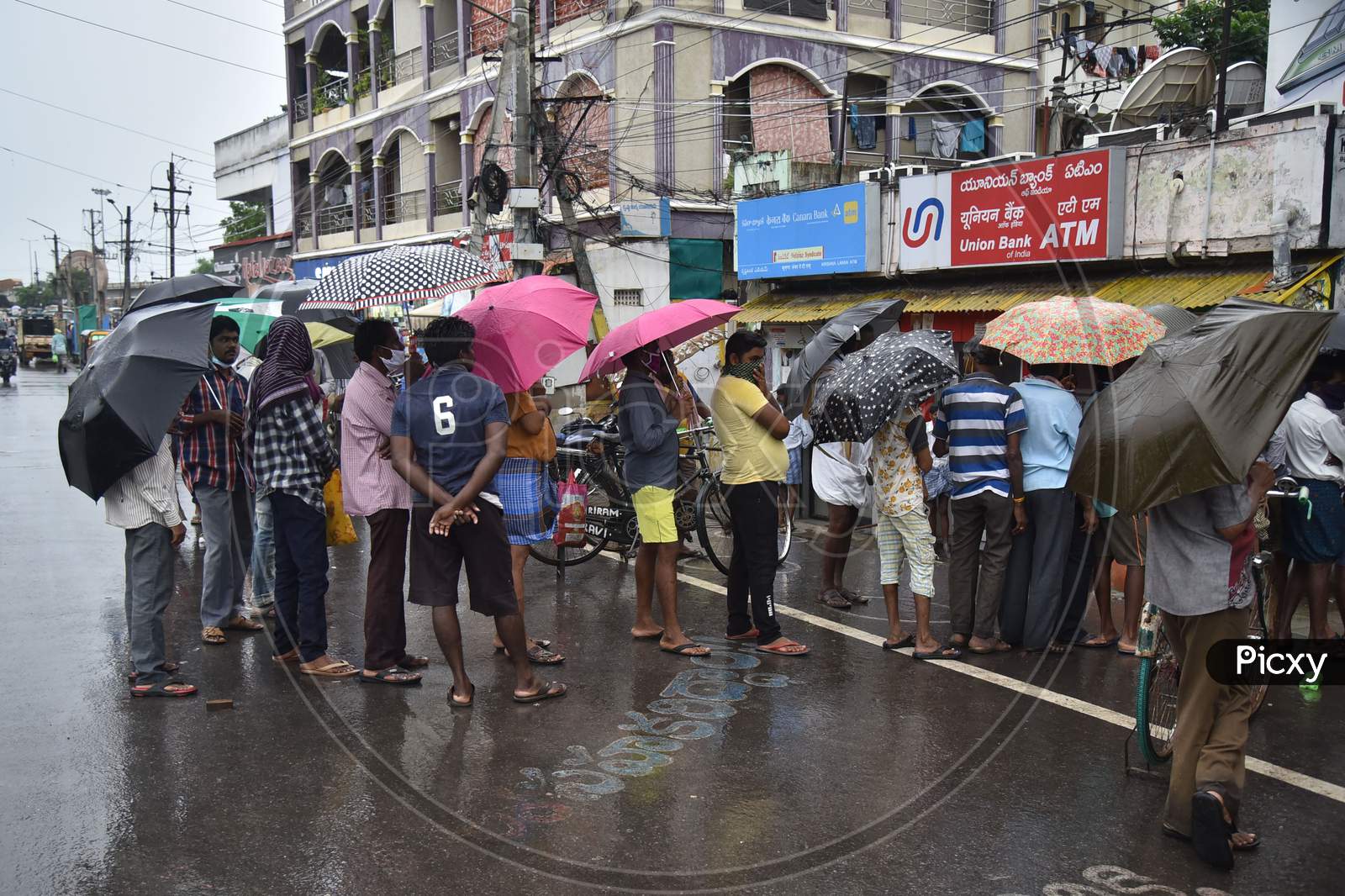 People Wait With Umbrellas During Rain At A Wine Store, In Vijayawada On August 14, 2020.