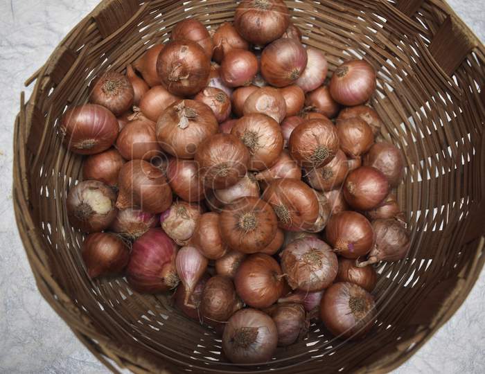 Top View Of Small Onions Stored In Round Brown Wicker Bamboo Basket In Indian And Pakistani Household.
