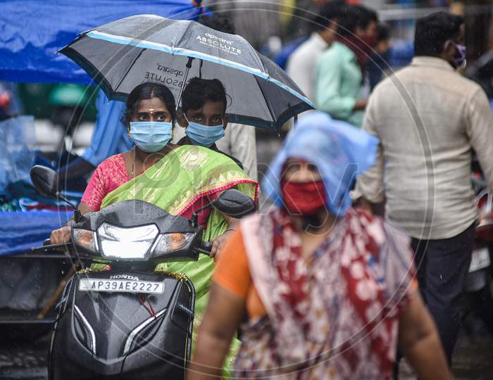 People Take Shelter Under An Umbrella While Riding A Vehicle, During The Rain, At Besant Road, In Vijayawada On August 15, 2020.