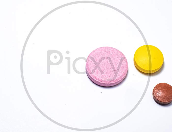 One White One Yellow And One Brown Pill On White Background.