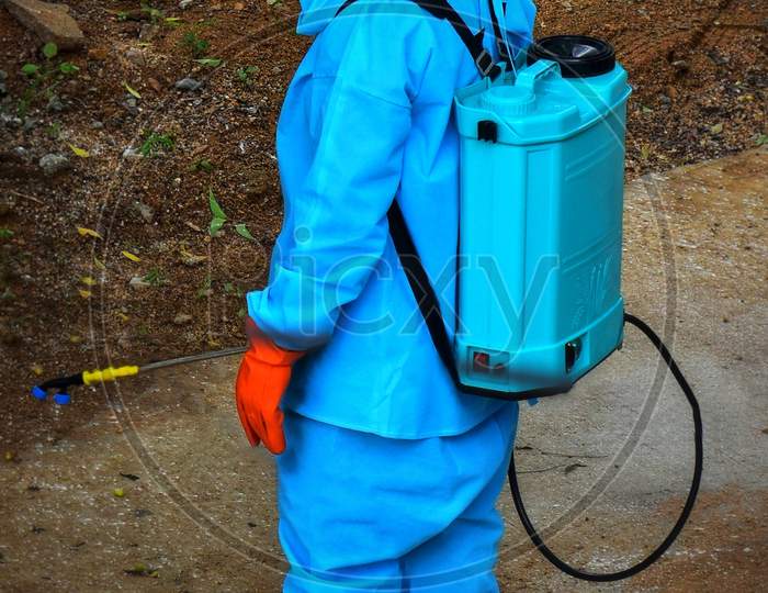 Worker In Blue Uniform And Face Mask Spraying Disinfectant Liquid To Sanitize A Locality