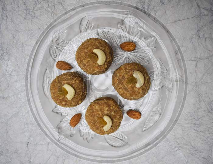 Top View Of Laddu, Ladoos Indian Sweet Balls On Transparent Crockery Plate Decorated With Almonds And Cashewnuts. For Festivals Like Ganesh Chaturthi
