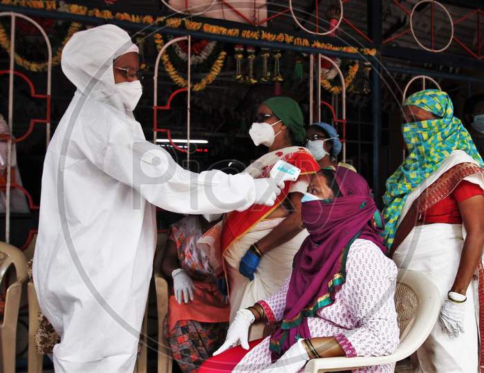 A healthcare worker wearing personal protective equipment(PPE) checks the temperature of a resident during a check up camp for the coronavirus disease (COVID-19) , at the entrance of a temple, in Mumbai, India on August 15, 2020.