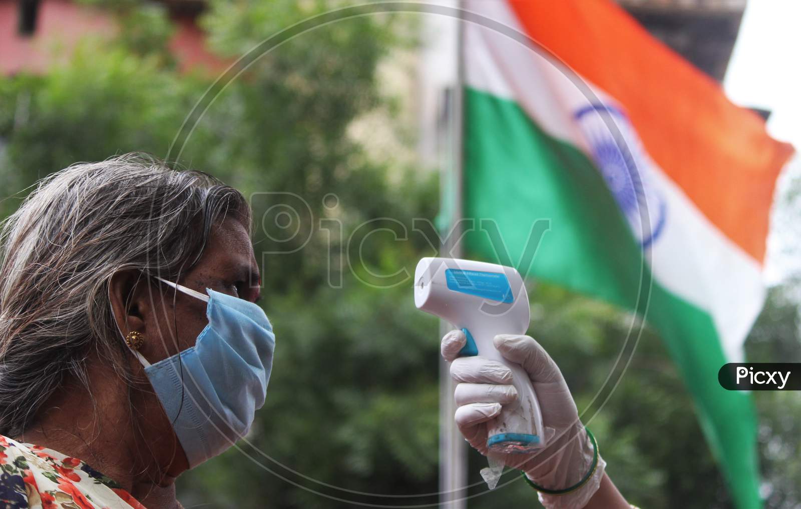 A healthcare worker checks the temperature of a resident during a check up camp for the coronavirus disease (COVID-19) , with the Indian Flag in the background, in Mumbai, India on August 15, 2020.