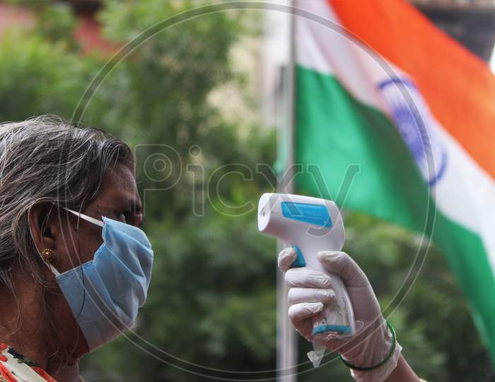 A healthcare worker checks the temperature of a resident during a check up camp for the coronavirus disease (COVID-19) , with the Indian Flag in the background, in Mumbai, India on August 15, 2020.