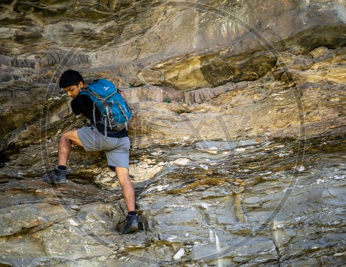 Young Boy Climbing The Rocks Wearing A Backpack.