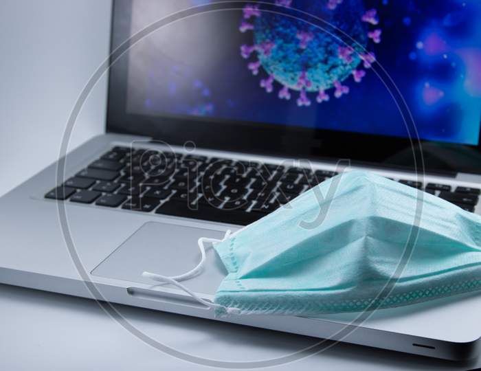 Protective surgical mask on top of computer with Covid-19 background. Working at home.