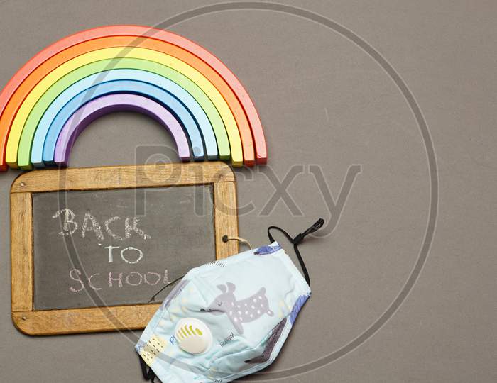 Top View Of Blackboard With Face Mask With Back To School Message And Rainbow. Back To School Concept With Covid 19. Flat Lay. Flat Design