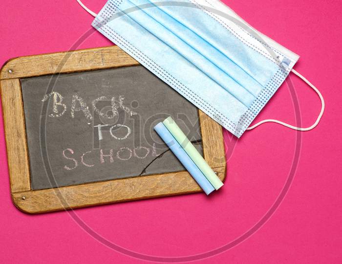 Top View Of Blackboard With Chalk Back To School Message And Face Mask. Back To School Concept With Covid 19. Flat Lay