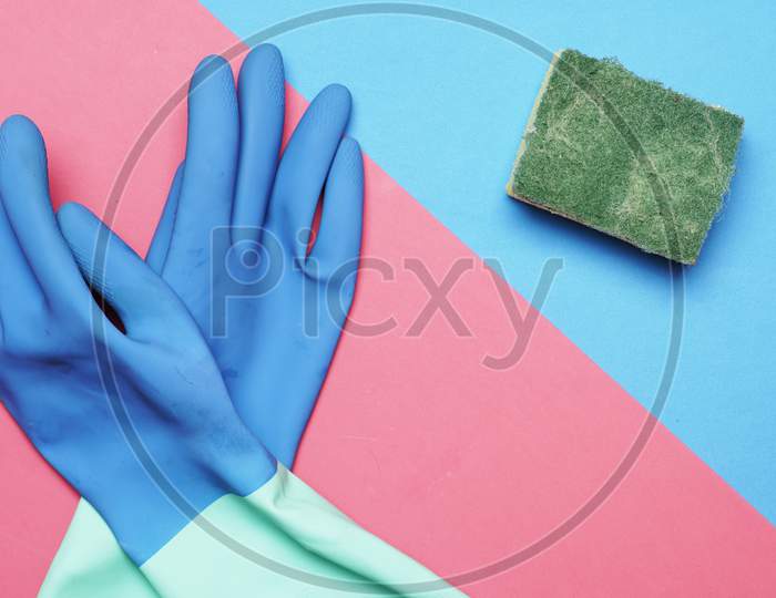 Flat Lay Of Cleaning Products On Blue And Pink Background Gloves And Scourer. Home Cleaning Concept.