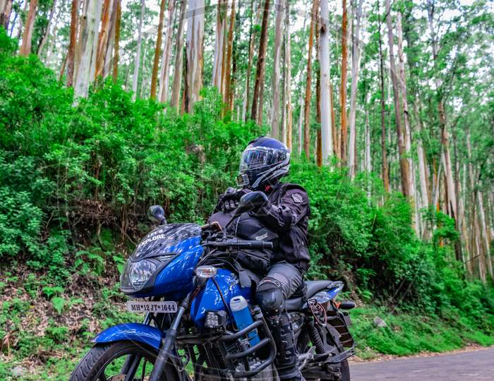 Motorcycle Rider Isolated On Empty Tarmac Road With Lush Green Forest