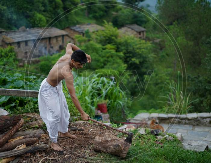 A Young Boy Wearing A White Dhoti Chopping Wood With An Axe.