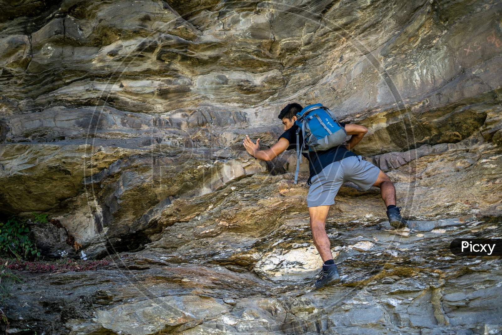 Young Boy Climbing The Rocks Wearing A Backpack.