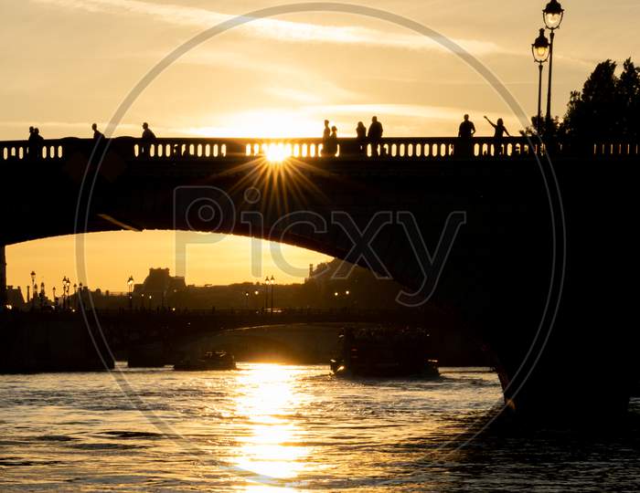 Silhouette Of Bridge Pont Au Change With People Over Seine River At Sunset In Paris, France.