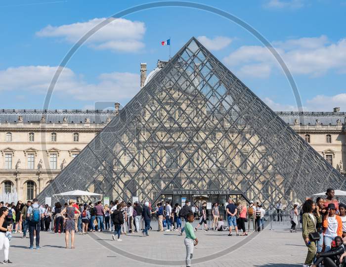 Louvre Museum Paris With Visitors At Bright Sunny Day.