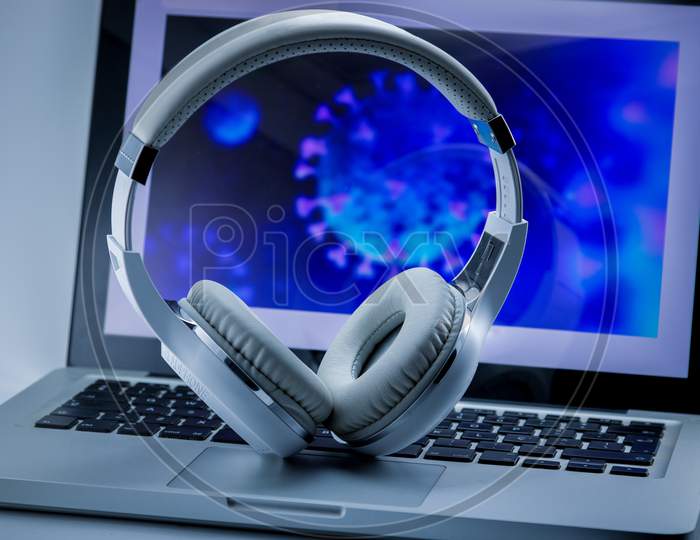 White design headphones with computer illustrating the Covid-19 virus. Work at home.