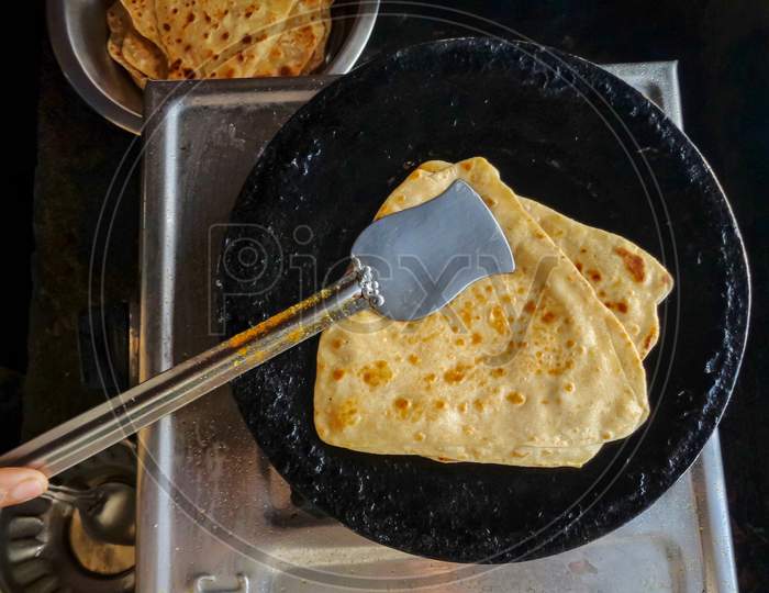 Indian traditional roti or paratha making in tawa on gas oven in indian kitchen