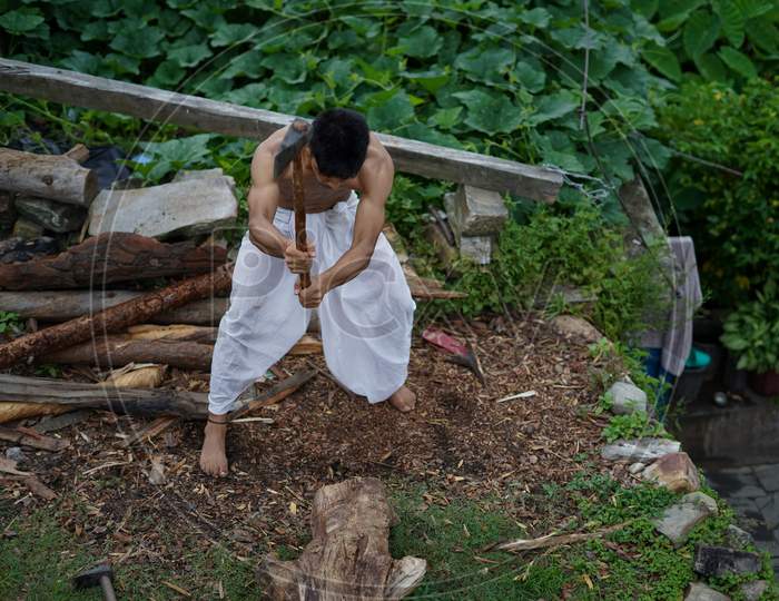 A Young Boy Wearing A White Dhoti Chopping Wood With An Axe.