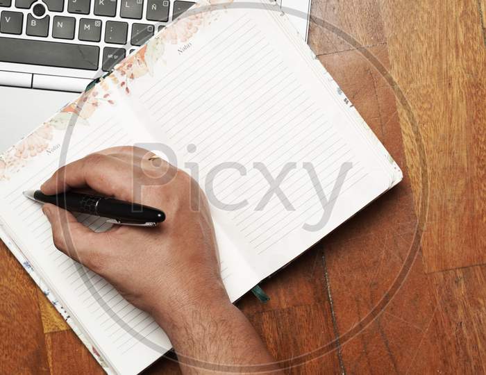 Work Table With Man'S Hand Writing On Agenda With Laptop. Flat Lay. Flat Design