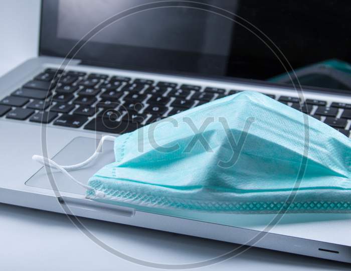 Protective surgical mask on top of computer with Covid-19 background. Working at home.
