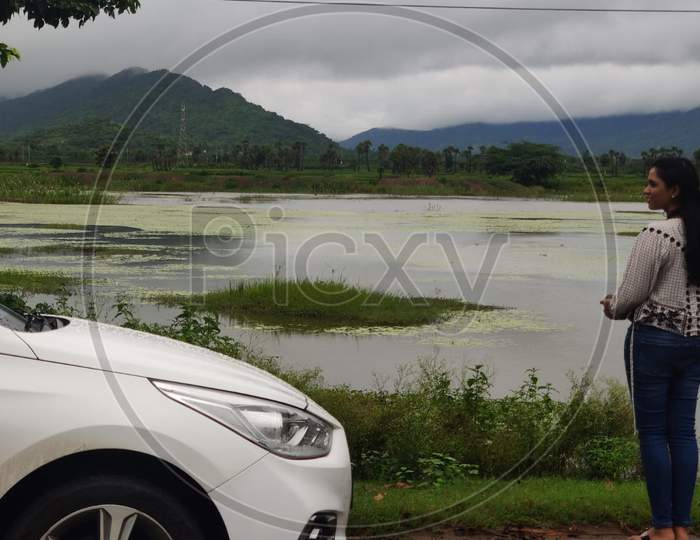 A girl enjoying the view of Lake mountains and hills beside car modern Indian