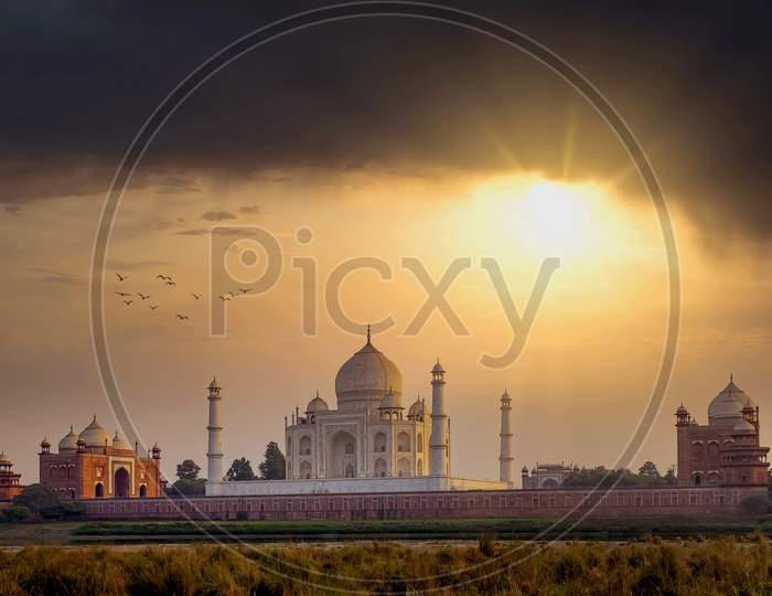 The white marble Taj Mahal building in a golden sunset as seen from across the Yamuna river in Agra, India.
