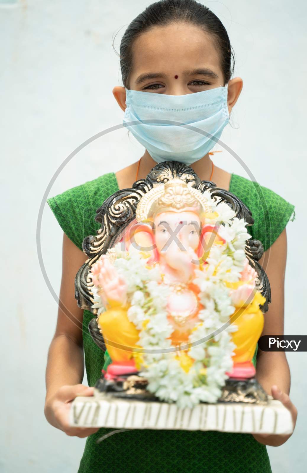 Girl Kid With Medical Mask Holding Ganesha Idol On Isolated Background - Concept Of Vinayaka Chaturthi Festival Celebrations During Coronavirus Or Covid-19 Pandemic