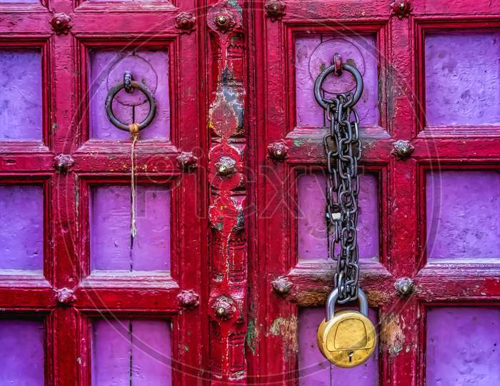 A brass lock and chains hanging on an antique red and pink wooden door in Varanasi, India