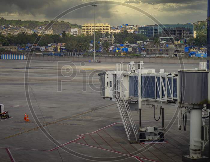 A Sky bridge at Chhatrapati Shivaji Maharaj International Airport and in the back ground local housing in old and new buildings to the fence line of the airport.