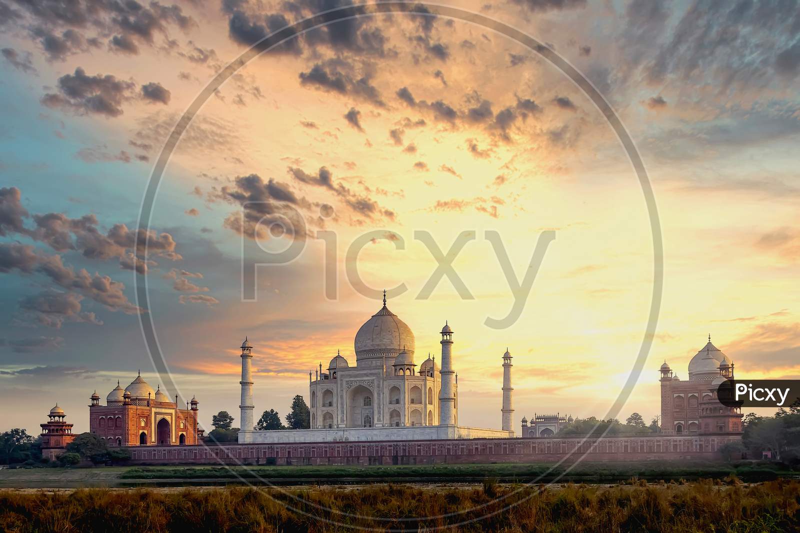 The white marble Taj Mahal building in golden light as seen from inside the red stone mosque in Agra, India