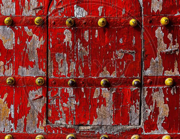 The Ramnagar Fort wooden entrance door in red and decorated with yellow spikes.
