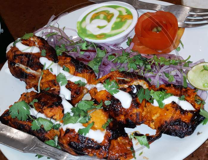 Chicken Tikka Kebab Served In A Plate with onion,green corriender,lemon,tomato and white-green chutney