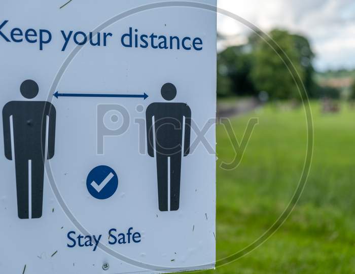 A Close Up Of A Sign In A Field Asking People To Socially Distance And Stay Safe At An Outdoor Event As The Coronavirus Lockdown Eases In England