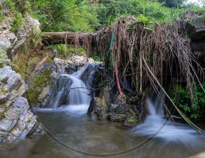 Slow Shutter Photo Of A Flowing River With A Broken Log On The Top Of It Forming A Bridge.