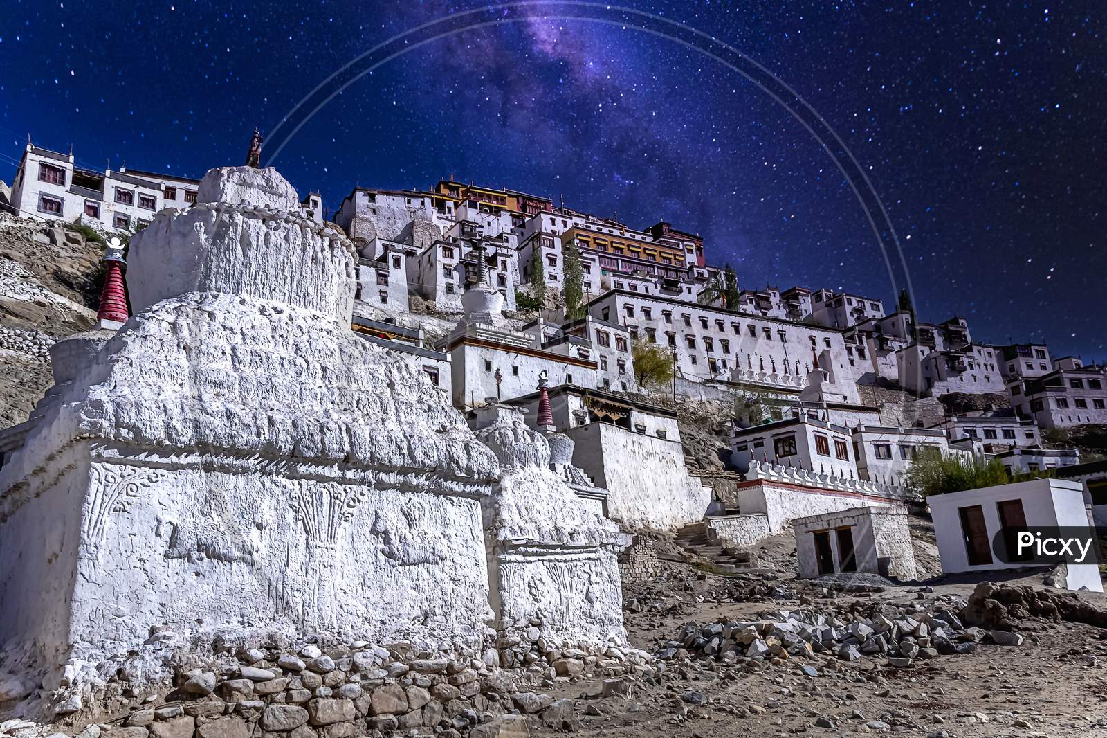 Seen from the Thiksey village you see white painted stupas holding buddhist relics under a starry sky as seen at the Thikse Monastery near Leh city, Ladakh, India
