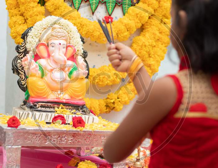 Kid Praying By Closing Eyes Infront Of God Ganesha Idol By Holding Or Offering Incense In Hand During Ganapati Festival Celebration At Home.
