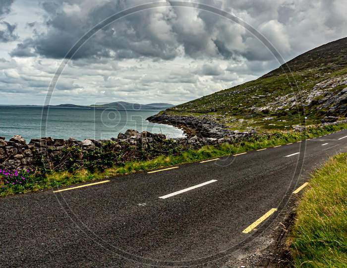 View Of The Rural Coastal R477 Road Between The Sea And The Rocky Area Of ​​The Burren, Geosite And Geopark, Wild Atlantic Way, Cloudy Spring Day In County Clare, West Coastal Of Ireland