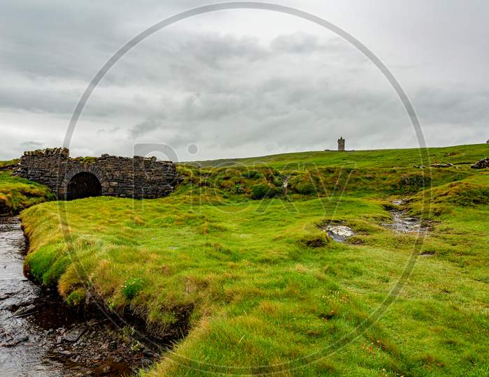 Irish Countryside Landscape With A Old Stone Bridge And The Castle Doonagore In The Background On The Coastal Walk Route From Doolin To The Cliffs Of Moher, Wild Atlantic Way, County Clare In Ireland