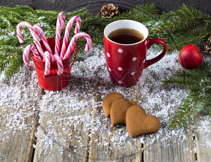 Christmas Tea, Cookies, Lemons, Mug, Heart Cookies On Decorations Table. New Year Celebration On Christmas. Christmas Sweet On Table. Christmas Candy Sticks In Red Tub.