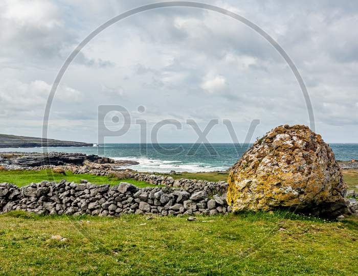 Irish Landscape Of A Giant Stone Next To A Stone Fence With The Sea In The Background Between Bothar Na Haillite And Fanore, Wild Atlantic Way, Wonderful Spring Day In County Clare In Ireland