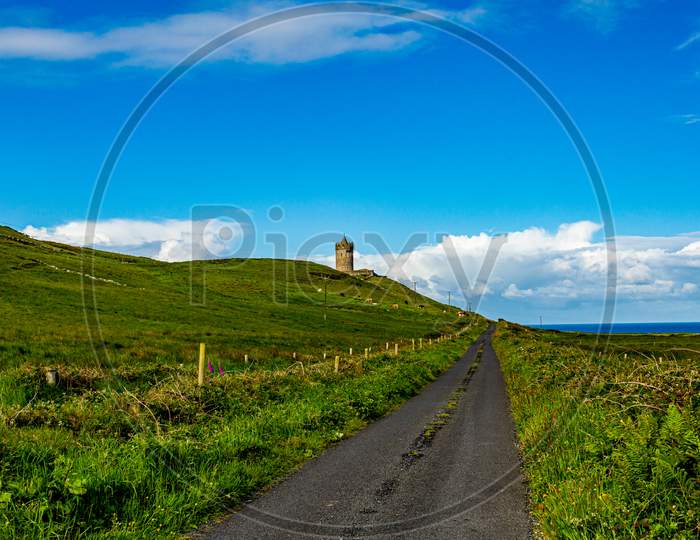 Beautiful Landscape Of A Road Between The Irish Countryside With The Doonagore Castle Tower In The Background In The Coastal Town Of Doolin, Wild Atlantic Way, Sunny Day In County Clare In Ireland