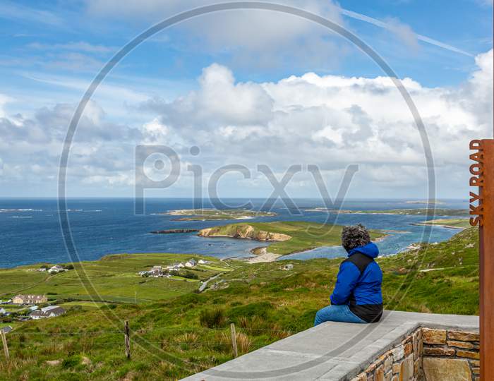 Sky Road Lookout With A Female Tourist In Blue Jacket Admiring The Scenery Of The Irish Countryside And The Atlantic Ocean, Sunny Spring Day In Clifden, County Galway, Ireland