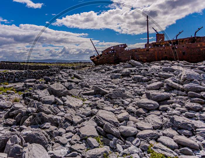 Stunning View Of The Rocky Beach Of Inis Oirr Island With Stone Fences And The Plassey Shipwreck In The Background, Abandoned Ship, Old And Rusty With Time, Sunny Day In The Aran Islands, Ireland