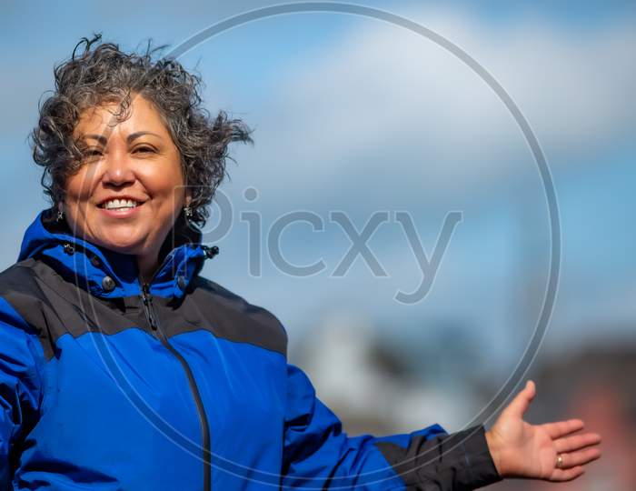 Beautiful Happy Mature Mexican Woman With Her Hair Tousled By The Wind With A Blue Jacket, Making A Sign Of A Very Good Day, Wonderful Sunny  Day To Enjoy Ireland