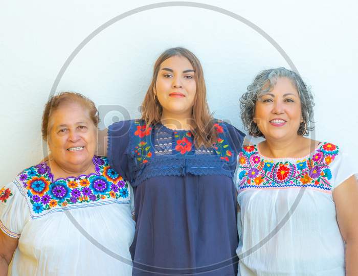 Three Generations Of Latin Mexican Women Smiling In Line, Daughter, Grandmother And Granddaughter Wearing Casual Clothes Looking At The Camera With A White Background, Space For Text