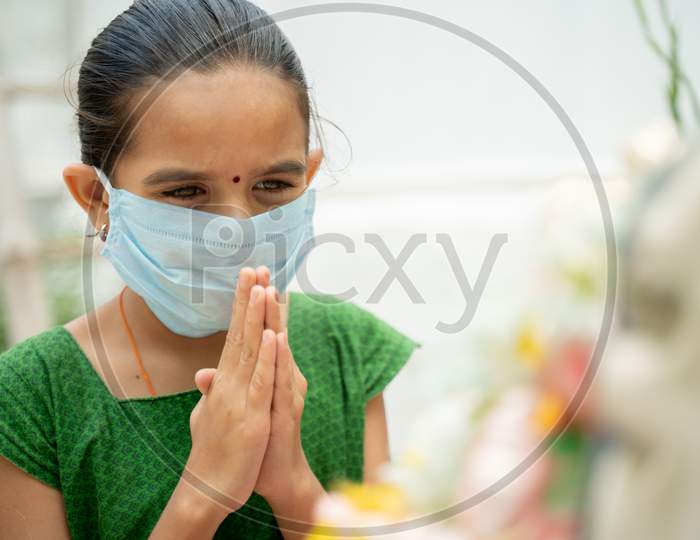 Young Girl Kid In Medical Mask Praying To God To Protect From Coronavirus Or Covid-19 By Folding Hands In Namaste Gesture.